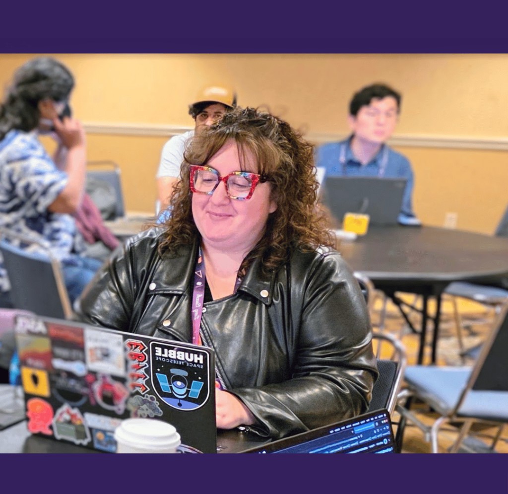 A pyOpenSci community member smiling while working on a sticker-covered laptop during PyCon US sprints.